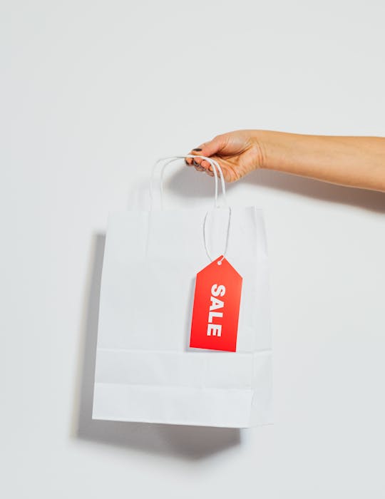 A person's hand holding a white shopping bag with a red sale tag on a white background.